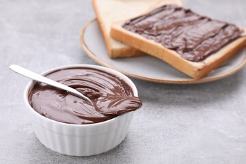 Tasty breakfast. Bowl with chocolate paste and sweet toasts on grey textured table, closeup