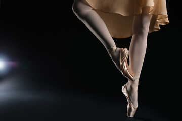 Ballerina in pointe shoes dancing on black background, closeup. Space for text