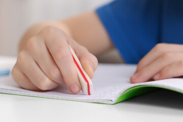 Boy erasing mistake in his notebook at white desk, closeup