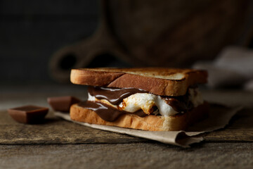 Delicious marshmallow sandwich with bread and chocolate on wooden table, closeup