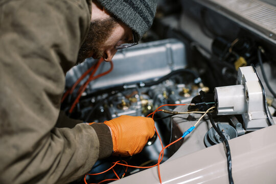 millennial man in winter clothing working on old car