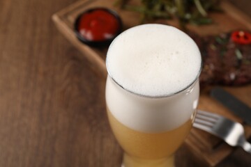 Glass of beer, delicious fried steak and sauce on wooden table, closeup. Space for text