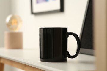 Black mug on white table indoors. Mockup for design