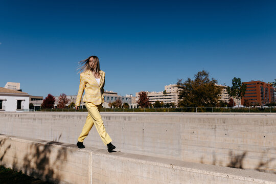 Stylish woman walking fast on concrete border