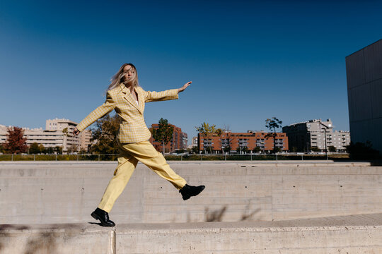 Stylish woman jumping on border during walk