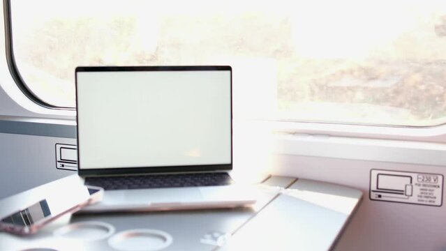 laptop with white screen in train moving wagon in the background trees flickering backlight space for text chromakey advertising next to the phone latest gadgets table in the train road trip