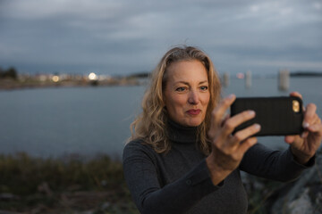 Woman taking photos with cell phone at sunset.