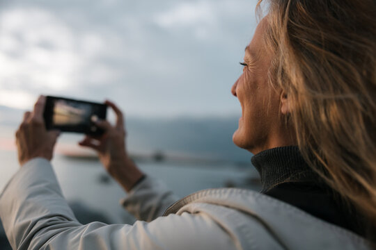 Woman taking photos with cell phone at sunset.