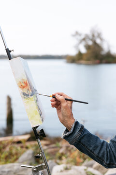 Silver haired woman painting on canvas by the river.