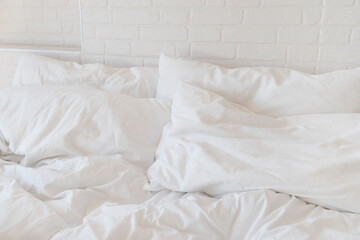 white bed sheets and pillows and white brick wall