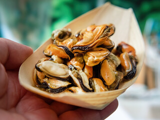 Tasty grilled mussels in a wooden paper bowl