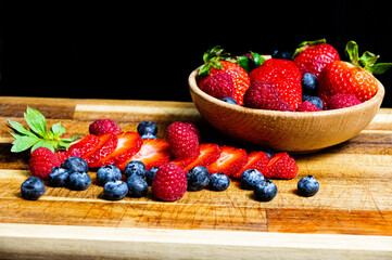 Sliced and raw berries in a wooden bowl and on a wooden table next to cutlery