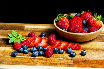 Sliced and raw berries in a wooden bowl and on a wooden table next to cutlery