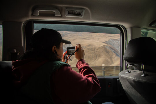 A woman sits in the car and takes a photo of mountains