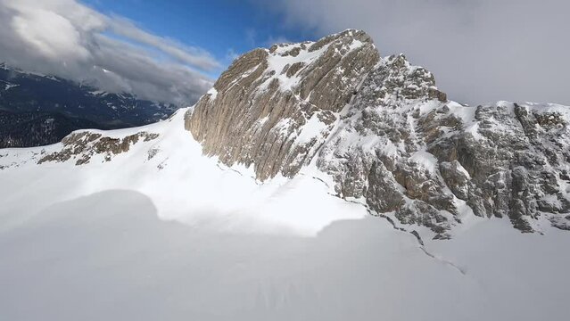 FPV sport drone raising shot to winter mountain peak cliff summit structure stone ridge snow valley frozen scenery aerial view. Rocky terrain texture north crag panorama exploration sky landscape 4k