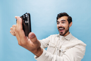 Portrait of a stylish man brunette surprise and open mouth looks at the phone blogger with a beard, on a blue background in a white T-shirt and jeans, copy space