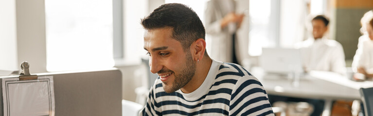 Obraz premium Businessman in casual clothes working laptop while sitting in modern office on colleagues background