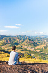 Man feeling good and calm sitting on top of a mountain while looking at the beautiful landscape of the valley. Person having thoughts and reflections while resting.