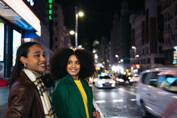 Young women waiting to cross a crosswalk in the city at night