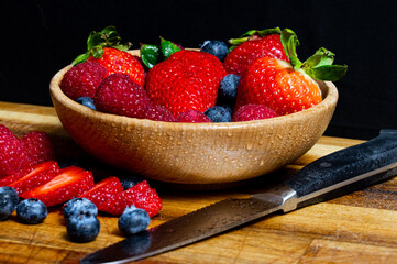 Sliced and raw berries in a wooden bowl and on a wooden table next to cutlery