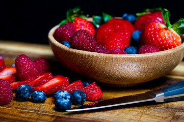 Sliced and raw berries in a wooden bowl and on a wooden table next to cutlery
