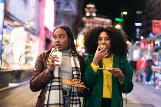 Young black women eating fast food on the street at night - Powered by Adobe