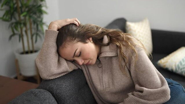 Young beautiful hispanic woman sitting on sofa with stressed expression at home