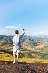 Traveler taking a selfie with his cell phone or smartphone to post on social media, with a landscape of mountains in the background.