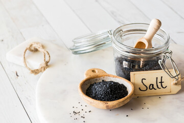 A jar and bowl filled with black Hawaiian rock salt on a marble slab.