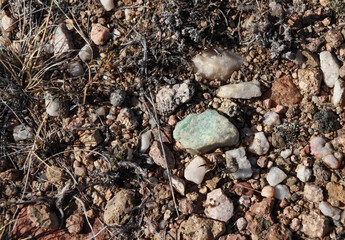 An assemblage of rocks scattered across the ground that includes a piece of green quartz. 