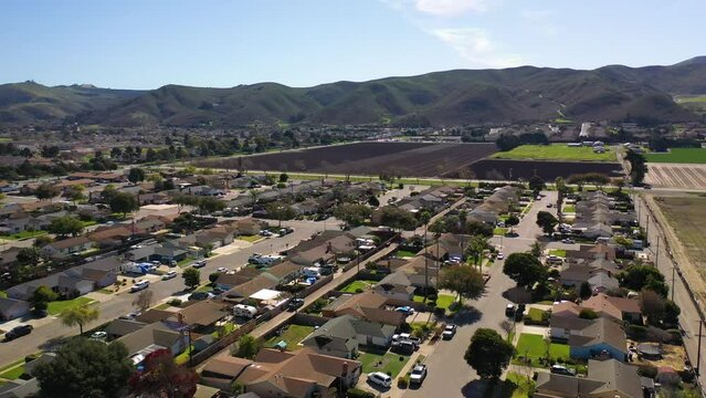 2023 - Excellent aerial footage of cars driving through a residential area by farmland and mountains in Lompoc, California.