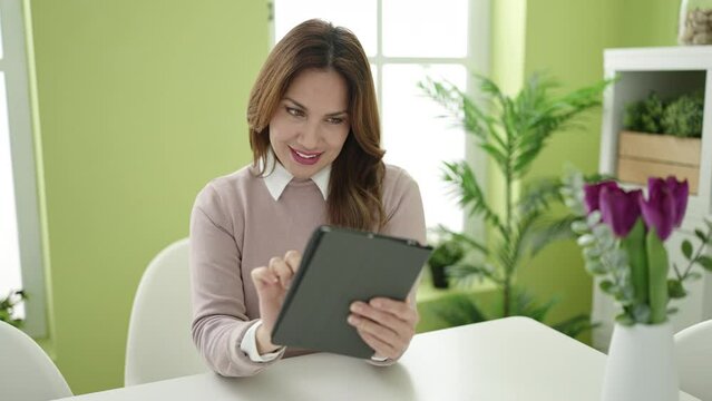 Young beautiful hispanic woman using touchpad sitting on table at home