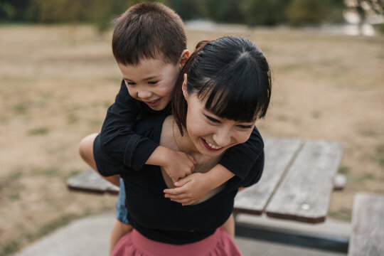 Mom giving shoulder ride to toddler son outside.