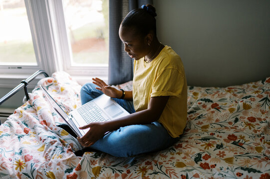 Smiling black girl sitting on her bed in her teenage room on laptop 