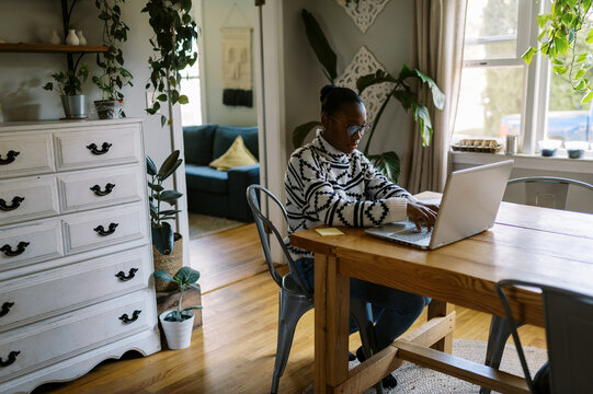 Black girl at home at kitchen table doing homework with laptop 