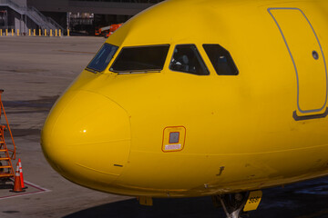 Obraz premium A close up image of a bright yellow airplane waiting on the tarmac at an airport with a pilot sitting inside of the cockpit of the jet.