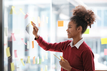 African American female employee write down on colorful sticky notes manage list, concentrated...