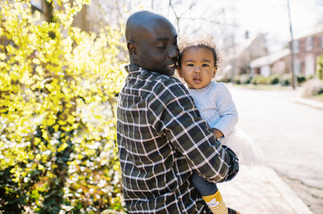 Smiling black dad holding his adorable toddler girl in arms