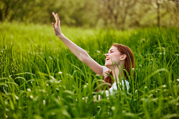 Naklejka na ściany i meble happy, contented woman sitting in tall green grass enjoying a pleasant day with her arms raised high