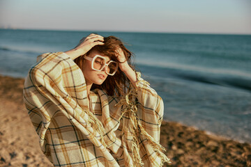 portrait of a woman in large glasses, wrapped in a blanket on the sea coast, holding her hair in the wind