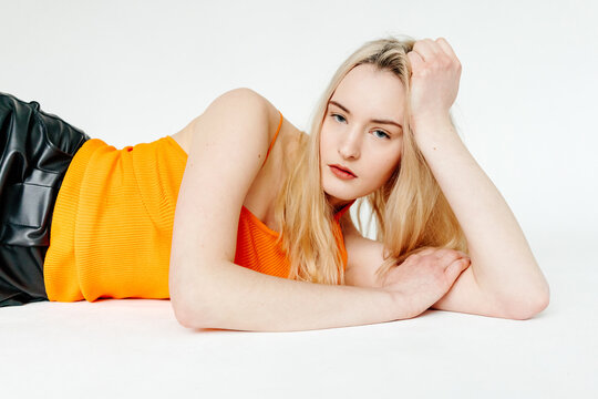 Serious female millennial in orange top lying on floor in studio