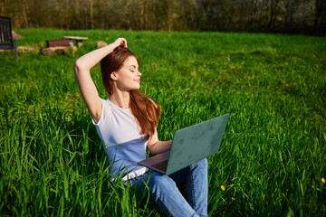 on a clear sunny day, a happy woman works sitting at a laptop in the field