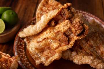 Chicharron. Crispy Fried pork rind, are pieces of aired and fried pork skin, traditional Mexican ingredient or snack served with lime juice and red hot sauce. Closeup.