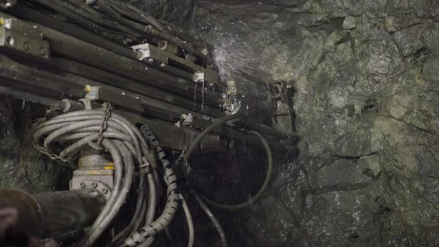 Machinery equipment drills large hole in hard rock of ore mine to set explosives. Robot drill with coolant operates spraying cold water closeup