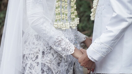 couple gently holding hands in bridal attire. bridal hands with elegant wedding rings with white...