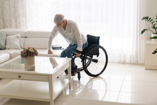 Woman Moving From Wheelchair To The Sofa At Home