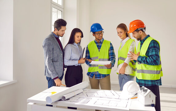 Team of diverse male and female architects and engineers discussing construction plan. Group of multiracial men and women in suits or hard hats and uniforms looking at blueprints during office meeting - Powered by Adobe