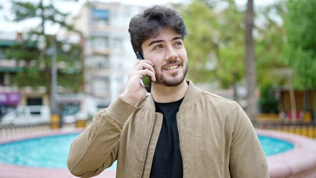 Young hispanic man talking on smartphone smiling at park