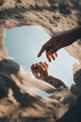 A woman's hand touches the reflection in the mirror on the beach