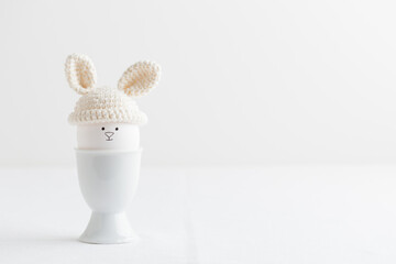 Easter egg in crochet hat with bunny ears in egg holder on white